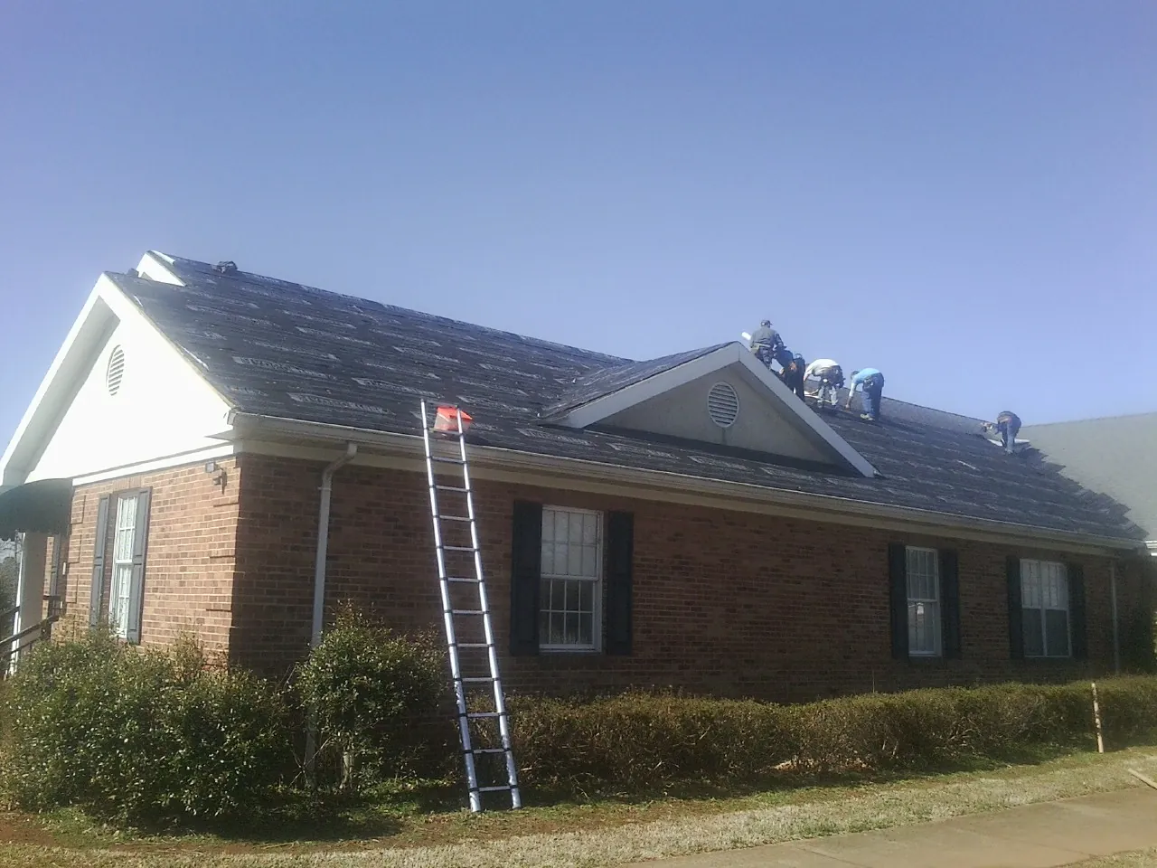 Crew tearing shingles off a brick ranch roof with a ladder set — Metal Roof Repair work by our crew in Newport Coast
