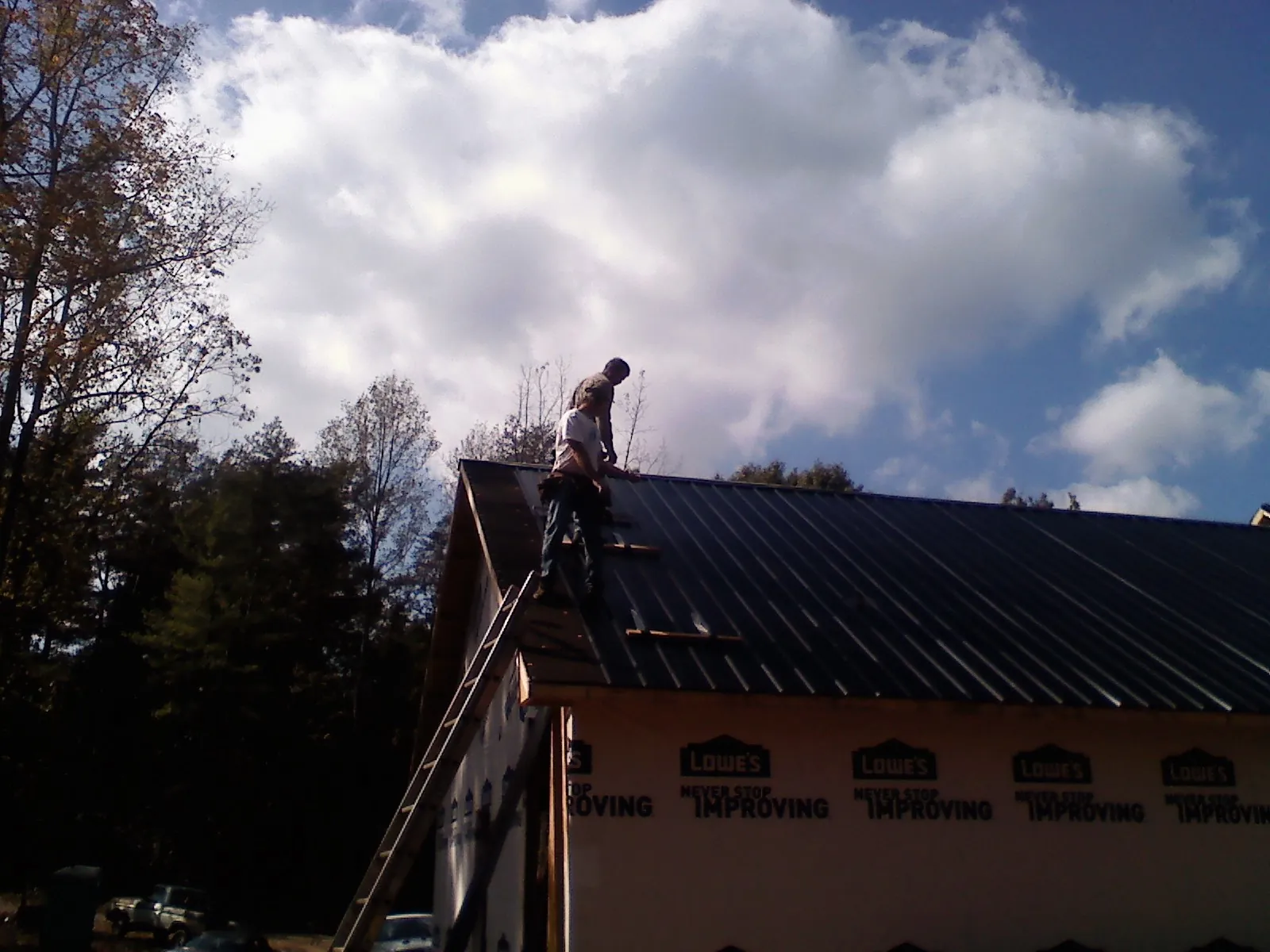 Roofer fastening dark metal panels high against a cloudy sky, from a Roof Inspection job in Newport Coast