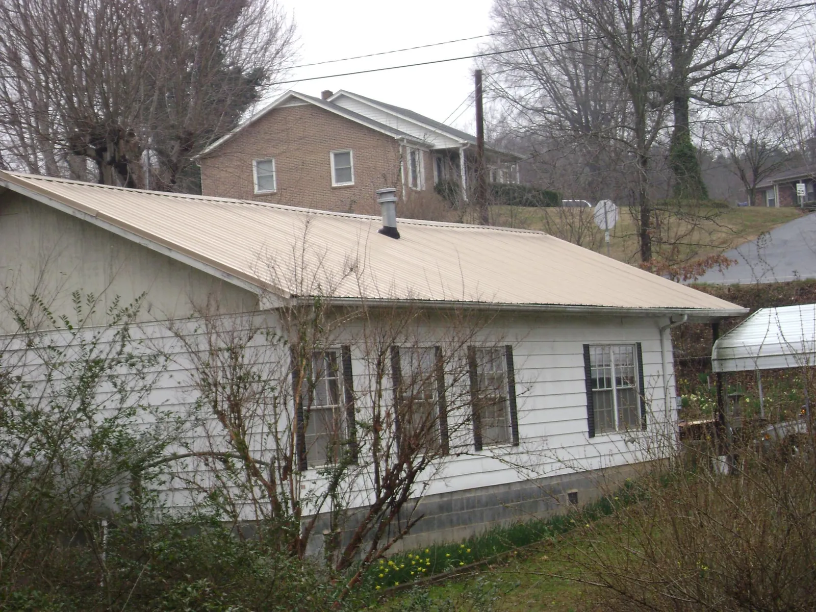 Tan metal roof on a white sided house set into a hillside — Commercial Roofing by Roofing Brothers in Newport Coast