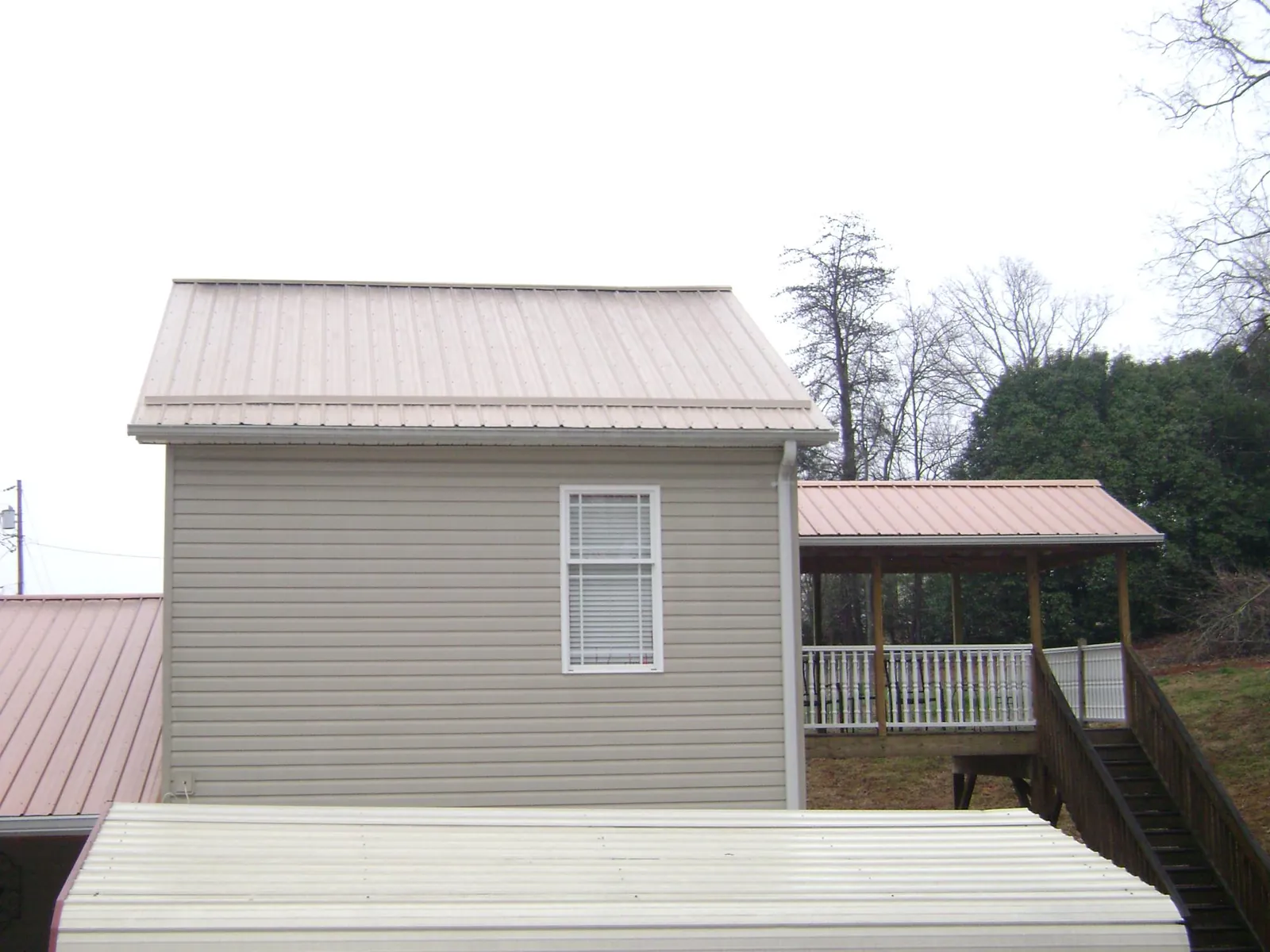 Tan metal roofs on a two story addition and attached porch, from a Roof Replacement job in Newport Coast
